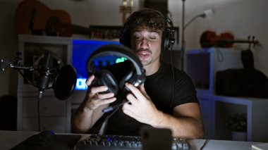 Yakışıklı İspanyol bir adam, heyecan verici bir oyun akışına kapılmış, oyun odasının parıltıları arasında sanal sohbete dalmış, kulaklıkları emirlere hazır.