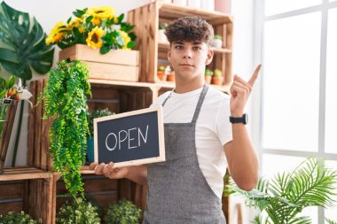 Çiçekçi dükkanında çalışan İspanyol genç elinde açık tabela, gülümsüyor. 