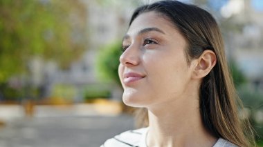 Genç, güzel, İspanyol bir kadın, gülümsüyor. Parkta kendine güveniyor.