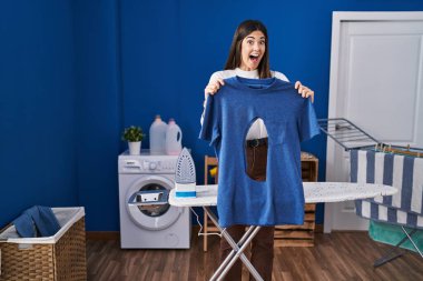 Çamaşır odasında ütü yapan genç esmer kadın çılgın kutlamalar yapıyor ve gözleri açık heyecanla bağırıyor.. 