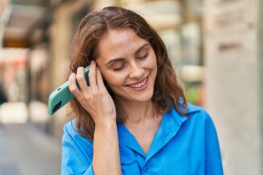 Caddedeki akıllı telefondan kendine güveni tam bir sesli mesaj dinleyen genç bir kadın.