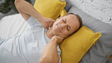 Mutsuz orta yaşlı bir adam, ciddi şekilde yaralanmış, boyun ağrısı çekiyor, yatakta uzanıyor, yatak odasının yalnızlığında sessizce acı çekiyor.