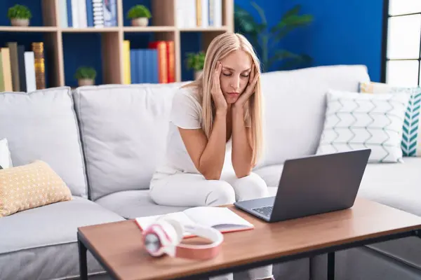 Young blonde woman student stressed sitting on sofa studying at home