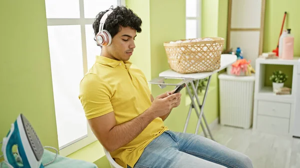 Young latin man listening to music waiting for washing machine at laundry room