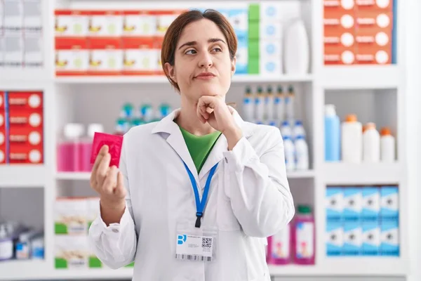 Brunette Woman Working Pharmacy Drugstore Holding Condom Serious Face Thinking — Stock Photo, Image