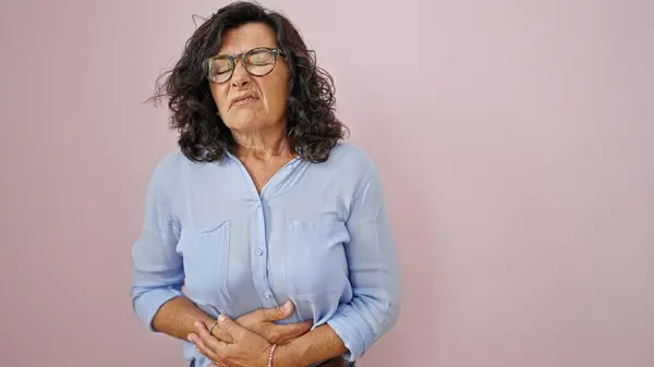 Middle age hispanic woman suffering for stomach ache standing over isolated pink background