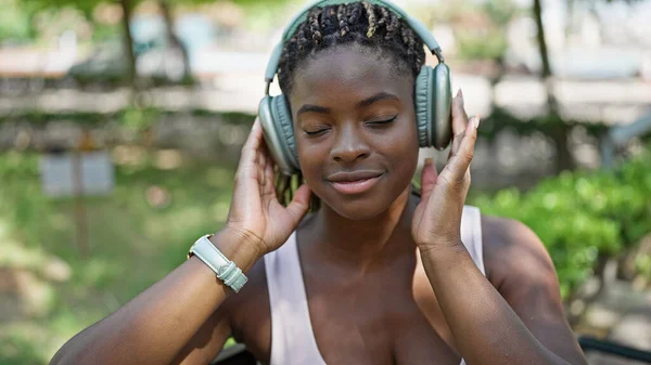 African american woman listening to music relaxed on bench at park