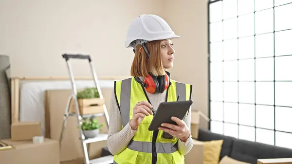 Young blonde woman architect using touchpad with serious expression at new home