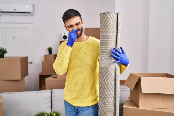 Young hispanic man smelling dirty carpet at new home