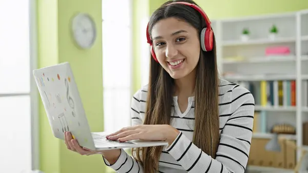 Young beautiful hispanic woman student smiling confident using laptop and headphones at library university