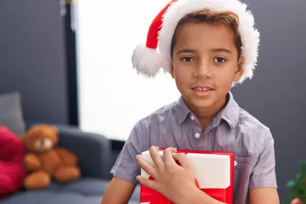 愛らしいヒスパニックの少年は自宅に立っているクリスマスの贈り物を抱きしめます — ストック写真