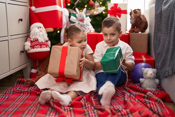 Δύο Παιδιά Που Κρατούν Δώρα Στο Πάτωμα Δίπλα Στο Χριστουγεννιάτικο — Φωτογραφία Αρχείου