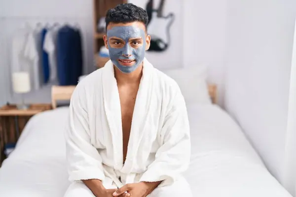 Young latin man relaxed on bed with facial mask treatment at bedroom