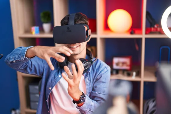 Young hispanic man streamer playing video game using virtual reality glasses at gaming room