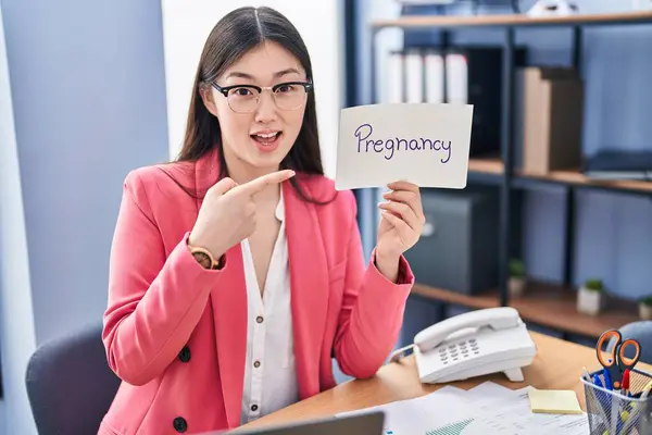 中国的年轻女性在办公室里拿着怀孕的标志微笑着 手指手画脚地微笑着 — 图库照片
