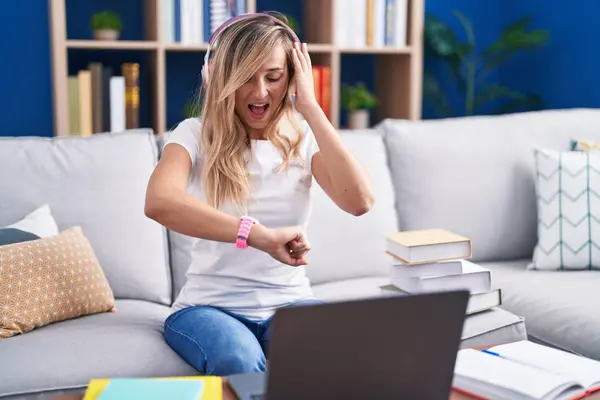金髪の若い女性は 時計の時間を心配して家でコンピュータのラップトップを使用して勉強 遅れることを恐れています — ストック写真