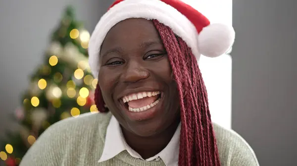 African woman with braided hair smiling by christmas tree at home