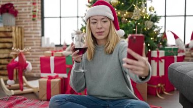 Mutlu genç bir kadın, şarap içerken ve Noel 'i evde kutlarken cep telefonuyla selfie çekiyor.