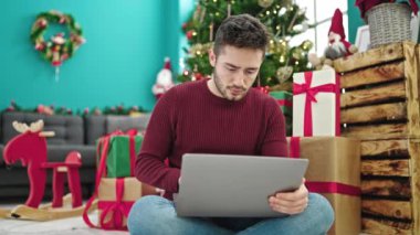 Evde dizüstü bilgisayarı olan genç adam Noel ağacına karşı.