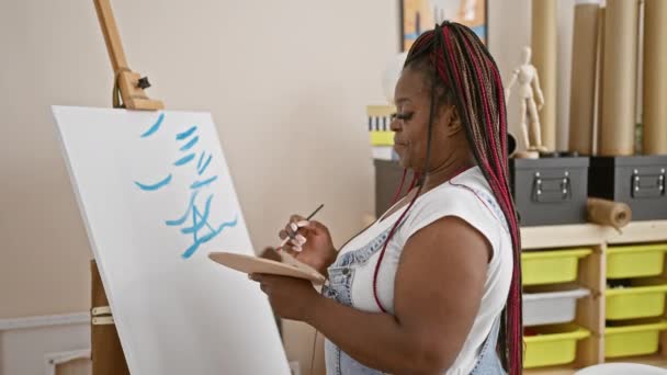 快乐的非洲裔美国女画家自信地画画 站在画布上时 在画室里灿烂地微笑着 拥抱着她的创造力 — 图库视频影像