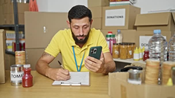 Νεαρός Ισπανός Εθελοντής Χρησιμοποιώντας Smartphone Κρατώντας Σημειώσεις Στο Φιλανθρωπικό Κέντρο — Αρχείο Βίντεο