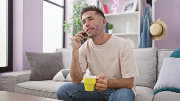 Joyful Young Hispanic Man Lounges Sofa Home Chatting Confidently Smartphone — Stock Video