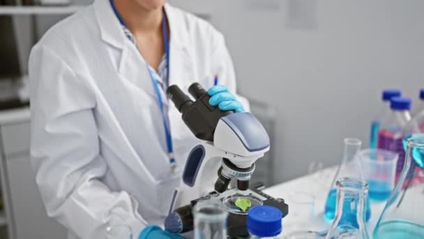 一位红头发的年轻女科学家笑着在一家高科技实验室的心脏地带用显微镜进行生物分析 — 图库视频影像