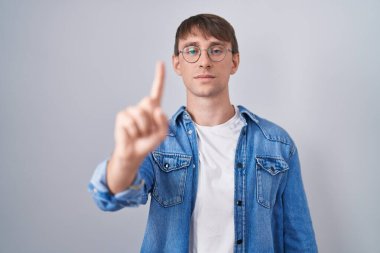 Kafkasyalı sarışın adam gözlüklü, parmağını kaldırmış ve kızgın bir ifade takınıyor. 