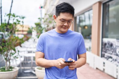 Genç Çinli adam kafeterya terasında akıllı telefon kullanıyor.