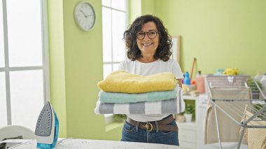 Orta yaşlı İspanyol kadın çamaşır odasında katlanmış havluları tutarken kendine güler.