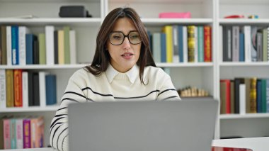 Kütüphanede dizüstü bilgisayar kullanan güzel İspanyol bir kız öğrenci.