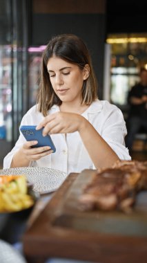 Genç, güzel, İspanyol bir kadın restoranda masada otururken mutlu bir şekilde gülümsüyor.