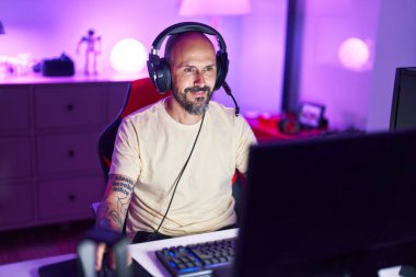 Young bald man streamer playing video game using computer at gaming room