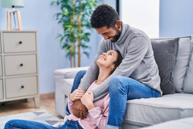 Erkek ve kadın çift evdeki kanepede oturup birbirlerine sarılıyorlar.