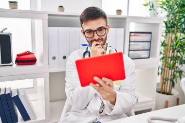 Klinikteki masada oturan dokunmatik ped kullanan genç İspanyol doktor.