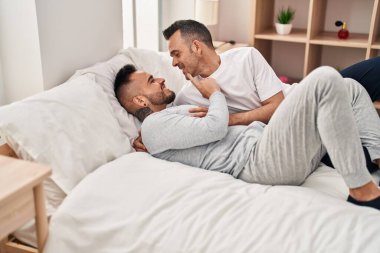 Two men couple lying on bed hugging each other at bedroom