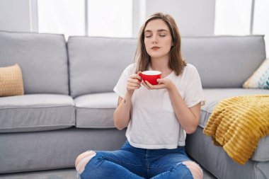Young woman drinking coffee sitting on floor at home