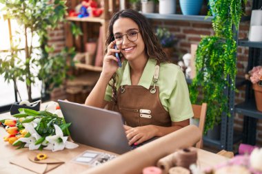 Çiçekçide dizüstü bilgisayar kullanarak konuşan güzel İspanyol çiçekçi kadın.