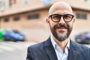 Genç kel iş adamı gülümsüyor. Kendine güveni tam caddede duruyor.