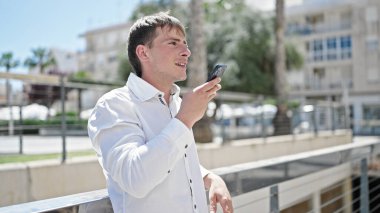 Young caucasian man sending voice message with smartphone at street