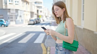 Sokakta akıllı telefon kullanan genç sarışın kadın.