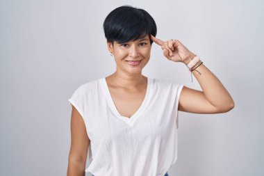 İzole edilmiş arka planda duran kısa saçlı genç Asyalı kadın tek parmakla gülümseyerek, harika bir fikir ya da düşünceyle, iyi bir hafızayla, 