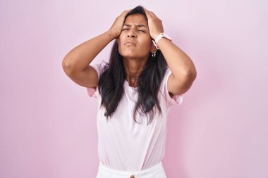 Pembe arka planda duran genç İspanyol kadın acı ve migren yüzünden çaresiz ve stresli baş ağrısı çekiyor. Eller başının üstünde.. 