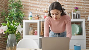 Genç ve güzel İspanyol kadın yemek odasında dizüstü bilgisayar kullanıyor.