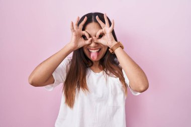 Pembe arka planda duran genç Arap kadın dürbün gibi jest yapıyor, gözleri parmaklarından bakıyor. çılgın ifade. 