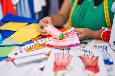 Terzi dükkanında elinde iplik ve renk testi tutan beyaz saçlı bir kadın.