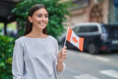Young beautiful hispanic woman smiling confident holding canada flag at street