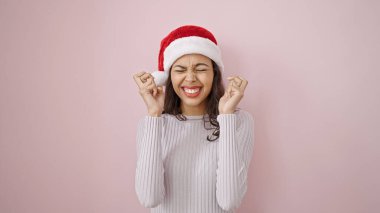 Genç ve güzel İspanyol kadın, izole edilmiş pembe arka planda noel şapkası takarak kutlama yapıyor.