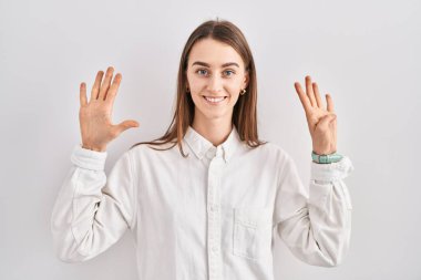 İzole edilmiş arka planda duran beyaz bir kadın dokuz numarayı gösterip işaret ederken kendinden emin ve mutlu bir şekilde gülümsüyor.. 