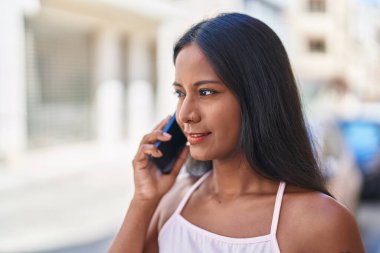 Genç, güzel bir kadın, gülümsüyor. Kendine güveniyor. Akıllı telefondan konuşuyor.